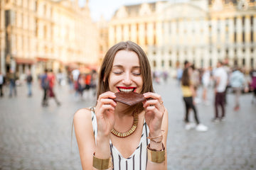 A young woman eating a bar of milk chocolate whilst standing in a plaza