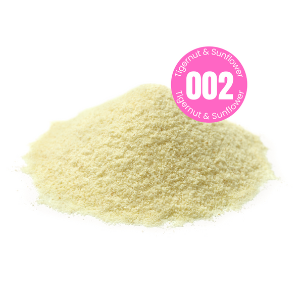 Product shot of a sweetened plant based milk powder.  A mound of an off white powder with a pink circular sticker label overlay with the recipe number 002 in the centre with the words Tigernut and Sunflower indicating the main ingredient of the powder.