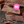 3 pieces of plant-based milk chocolate stacked on a black rough stone surface with smaller crumbled bits scattered in the foreground. The words 'milk chocolate made with’' in white text over the chocolate. The word milk is written with an exclamation mark indicating plant-based. Overlapping the chocolate is a pink circular sticker label overlay with text in white with 003 in the centre with the words Tigernut and Cashew indicating the recipe of the powder that was used to make this chocolate.